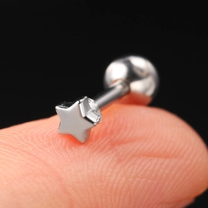 Macro shot of silver star-shaped zircon ear stud held on fingertip for size reference