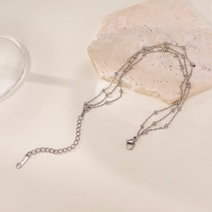 Detail of layered stainless steel anklet with beads on natural stone surface