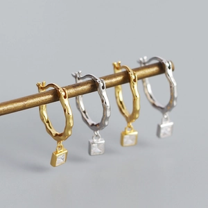 Detailed view of irregular silver and gold hoops with square zircon pendants on a stand