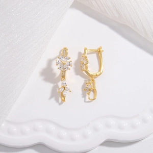 Elegant gold flower earrings with white zircon accents on a decorative white tray