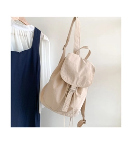 Dettaglio dello zaino in tela beige con coulisse appeso a una parete bianca pulita