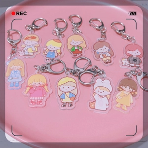 Flat lay of 10 acrylic cartoon girl keychains with silver D-clips in a pink tray