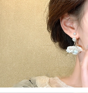 Dettaglio orecchini pendenti con perle e petali iridescenti indossati da una modella