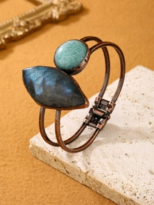 Detail of vintage copper bangle with natural labradorite and amazonite stones on travertine