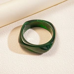 Macro detail of green resin geometric square bangle with marble texture on beige surface