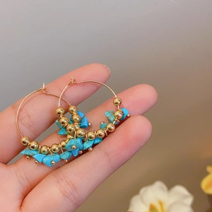 Detail of ethnic hoop earrings with gold beads and sky blue turquoise stones held by hand