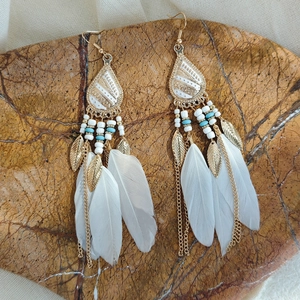 Macro detail of Bohemian feather earrings with blue beads and gold chain fringe