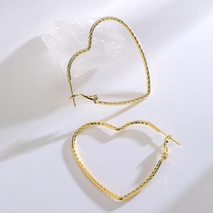 Minimalist heart-shaped gold hoop earrings with textured metal finish on white background