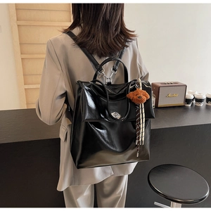 Detail of black glossy leather backpack with cute bear pendant and large capacity design