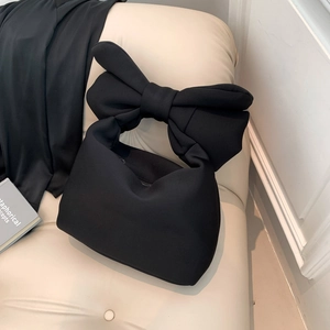Black padded nylon shoulder bag with a large bow handle on a beige leather sofa
