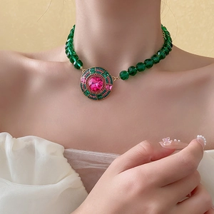Dettaglio di una collana vintage dorata con perle verdi e ciondolo di pietra rosa