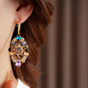 Close-up of vintage gold drop earrings with colorful gemstones worn by a model