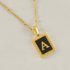 Macro shot of gold stainless steel necklace with black enamel pendant and letter A detail
