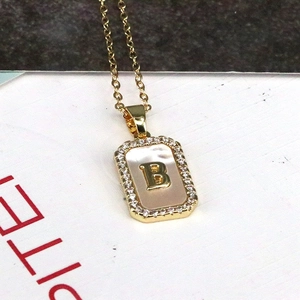 Detailed close-up of 18K gold letter B shell pendant necklace with sparkling zircon borders