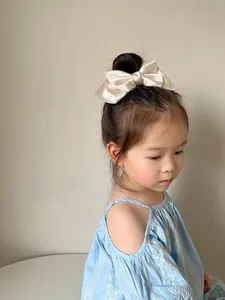 Detailed view of a large cream satin bow hair clip on girl with elegant silk texture