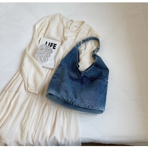 Flat lay of blue denim tote bag on a white dress creating a casual lifestyle look