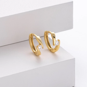 Macro shot of 925 silver gold-plated huggie earrings with round zircon on white stand