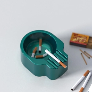 Gothic skull-shaped resin ashtray in metallic dark green finish with cigarette slot