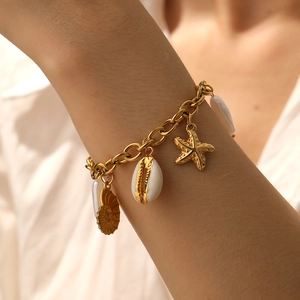 Detail of gold-plated chain bracelet with shell, starfish, and conch charms on wrist