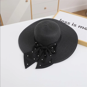 Detail of wide brim black straw hat with large bow and white pearls on white table