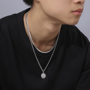 Detail of layered silver necklaces with a crown engraved round pendant on male model