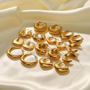 Assorted chunky gold stainless steel earrings on a soft cream satin fabric background