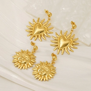 Detailed view of 18K gold plated heart and sunburst earrings on white marble and silk