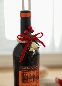 Close-up of Christmas wine bottle neck decoration with velvet bow, bells and red berries