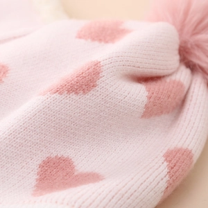 Nahaufnahme der rosa Strickmütze mit Herzmuster und flauschigem Bommel-Detail