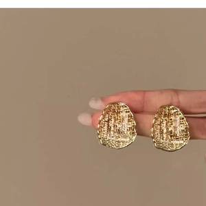 Detail showing hand-held gold plated oval stud earrings with fine woven mesh texture