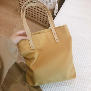 Detail of yellow canvas tote bag with beige leather handles and metal rivet reinforcement
