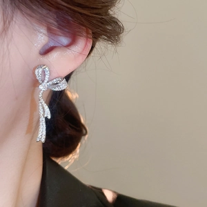 Detail of silver bow tassel earrings with sparkling cubic zirconia on model ear