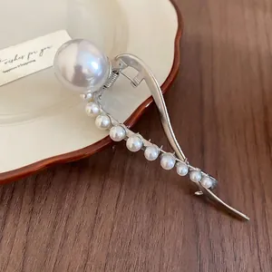 Elegant silver pearl hair claw clip with geometric curves on a ceramic tray