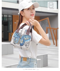 Detail of white embroidered handbag with a large blue butterfly and striped canvas handle
