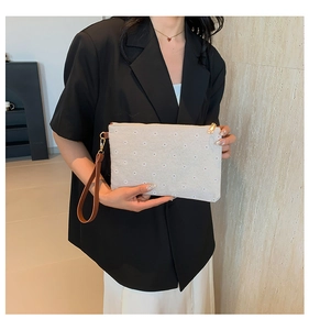 Detail of beige straw clutch bag with daisy embroidery, gold zipper and wrist strap