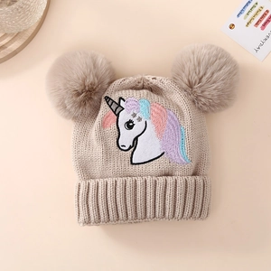 Close-up of beige knit baby hat featuring embroidered unicorn and fluffy double pom-poms