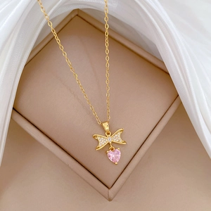 Close-up of gold titanium necklace with sparkling bow pendant and pink heart gemstone