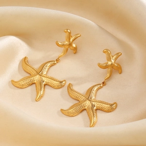 Golden double starfish dangle earrings on soft beige silk background with macro metal texture