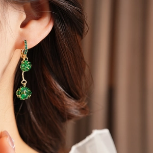 Close-up of vintage golden fringe earrings with green crystals worn by a model