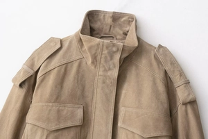 Detailed macro view of tan suede jacket featuring collar, epaulets and pocket stitching