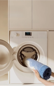 Detail showing machine washable blue and white plush bath mat being put into a laundry machine