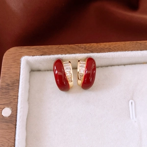 Detail view of 18k gold plated C-shaped earrings with red enamel and zircon stones