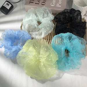 Flat lay of five sheer polka dot mesh scrunchies in pastel colors on a woven mat