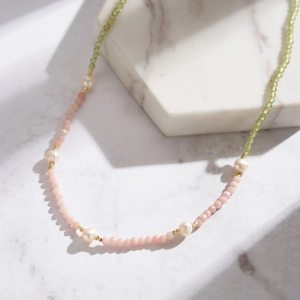 Detail of beaded necklace with pearls, pink and olive green beads on white marble