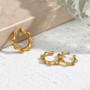Detailed view of three minimalist 18K gold-plated stainless steel wavy ear cuffs on marble
