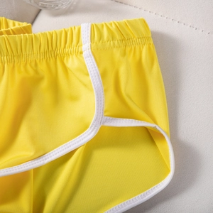 Seitendetail der gelben Sporthose mit weißem Kontrastsaum und elastischem Bunddesign