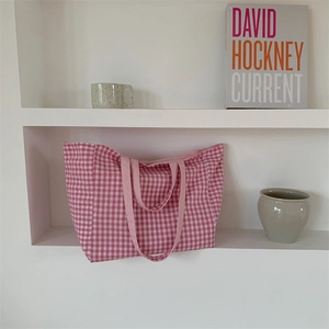 Pink plaid canvas tote bag in a minimalist setting with art books and ceramic decor