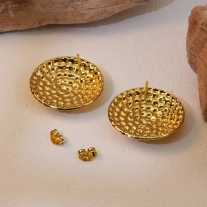 Detail of golden hammered round stud earrings with vintage texture on stone background