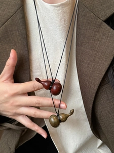 Detail view of wood gourd pendants in red-brown and green on a woven necklace
