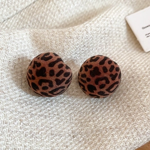 Detailed view of red leopard print flocked earrings on a soft beige knit fabric surface
